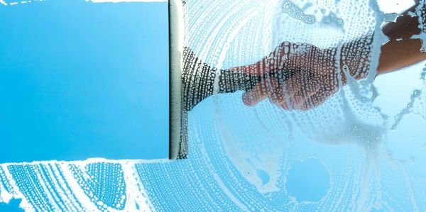 Hand cleaning a glass window with a squeegee and soap suds.