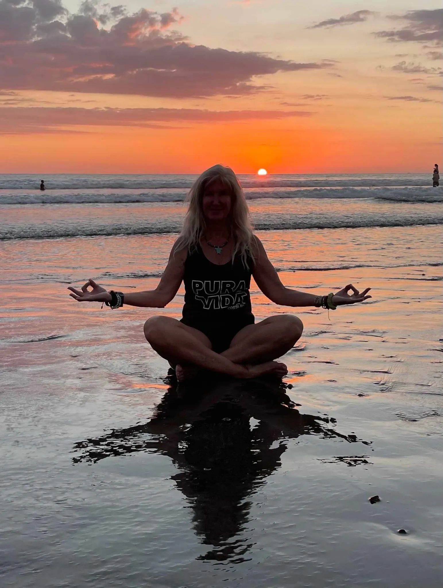 Person meditating on the beach at sunset with vibrant orange sky.