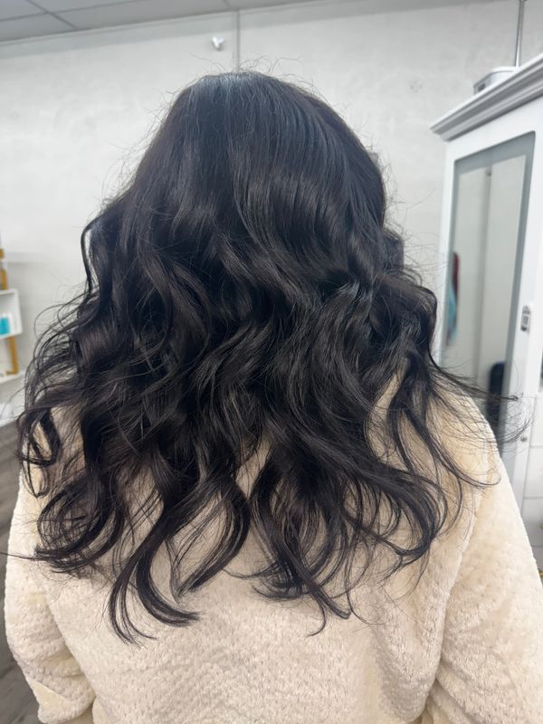 Wavy black hair cascading down a cozy beige sweater.