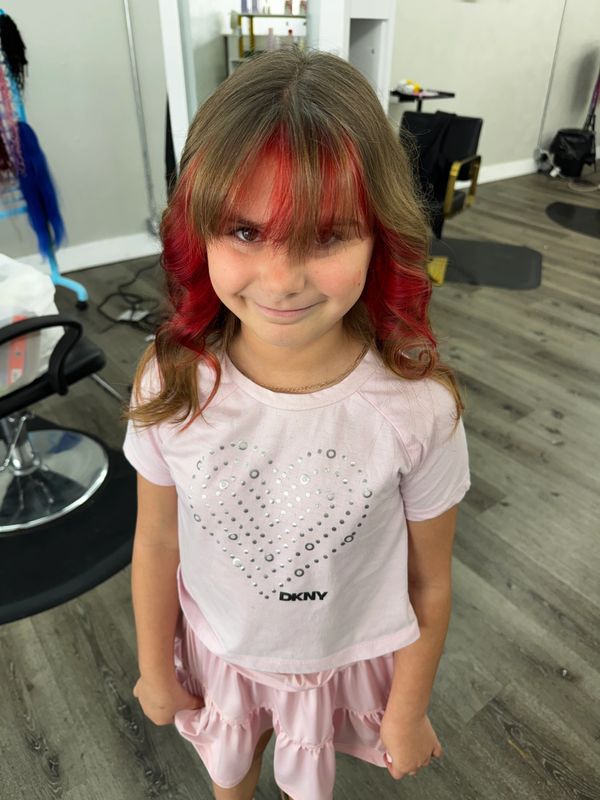 Young girl with red-streaked hair and a pink outfit smiles in a salon.
