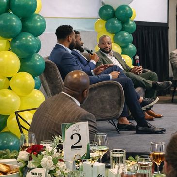 Panel discussion at a formal event with green and yellow balloon decorations.