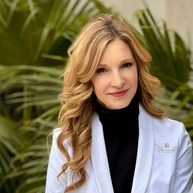 Woman with blonde hair in a white coat smiling.