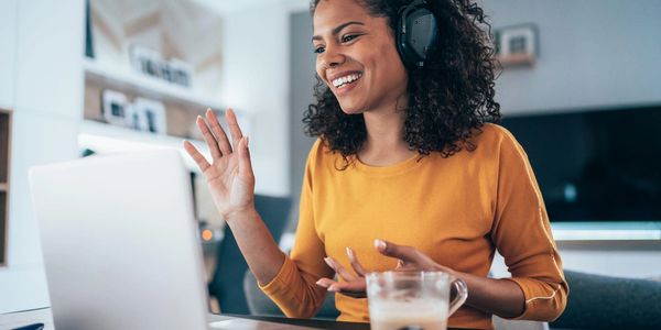 Woman happily video chatting on a laptop with headphones on.