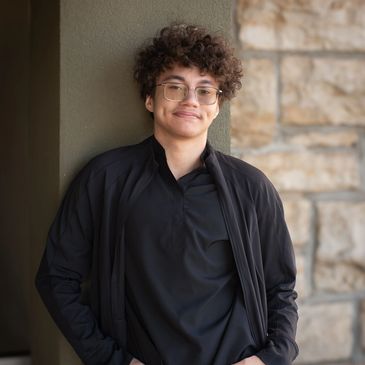 Young person with curly hair leaning against a wall, smiling.