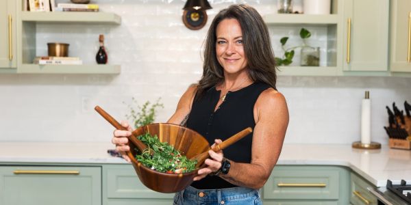 A woman holding a wooden bowl of fresh salad in a modern kitchen.