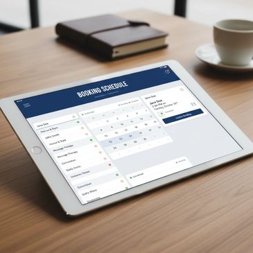 Tablet displaying a booking schedule app on a wooden table with a notebook and coffee cup.