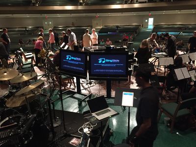 Musicians preparing in a concert hall with digital equipment and screens.