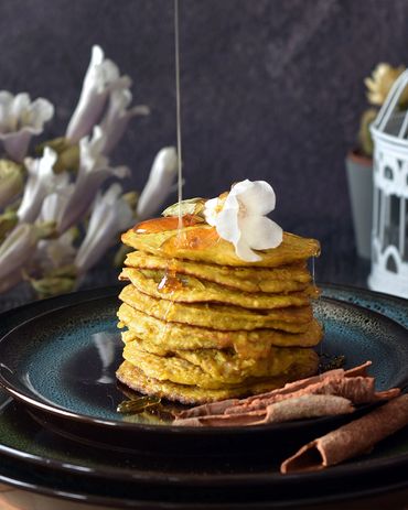 honey drizzling over a pancake stack with an edible flower and cinnamon sticks on a dark background 