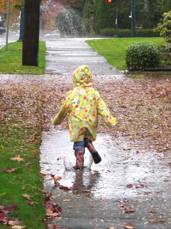 Child in a yellow raincoat splashing in a puddle on a rainy day.