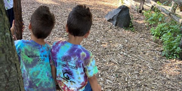 Two boys sitting outdoors wearing colorful tie-dye shirts.