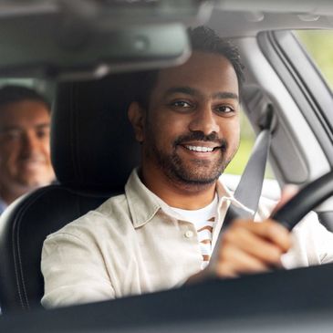 Smiling man driving a car with a passenger in the backseat.