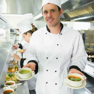 Chef presenting two bowls of soup in a professional kitchen.