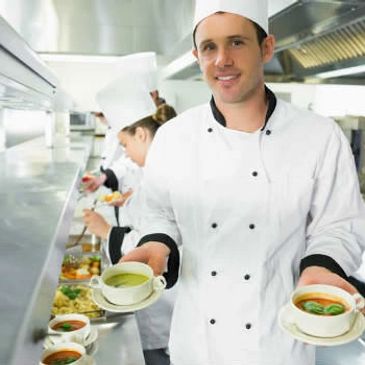 Chef presenting two bowls of soup in a professional kitchen.