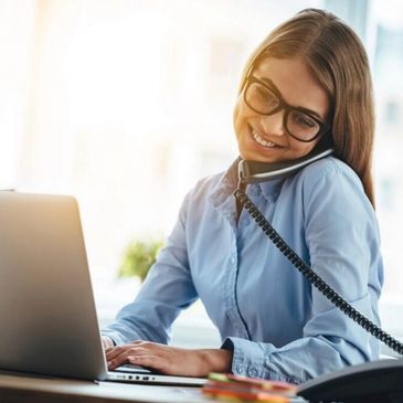Smiling woman multitasking with phone and laptop at work.