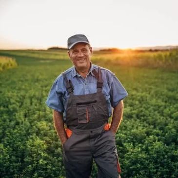 Smiling farmer standing in a green field at sunset.
