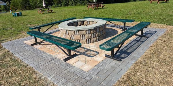 Outdoor fire pit area with green benches on a paved surface.