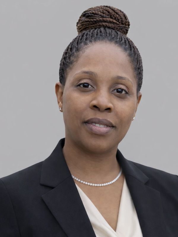 Professional woman with braided bun hairstyle wearing a black blazer and pearl necklace.