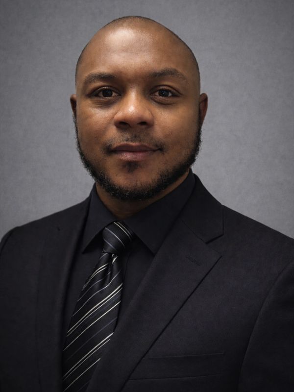 Professional headshot of a man in a black suit and striped tie.