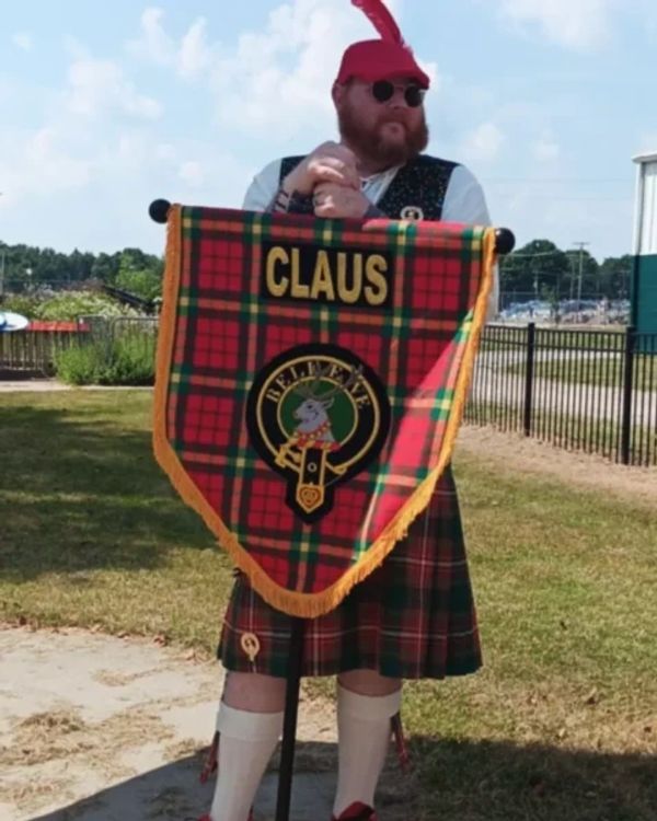 Man in traditional Scottish attire holding a tartan banner with 'CLAUS'.