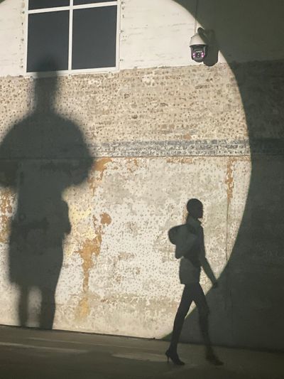 Person walking casting a large shadow on a wall.
