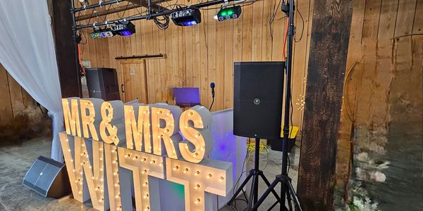 Illuminated MR &amp; MRS WITT sign at a rustic wedding venue.
