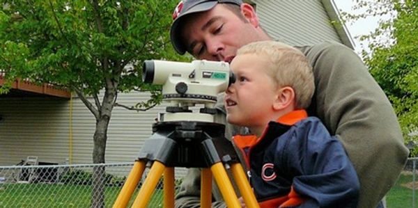 A man and young boy using a surveying instrument outdoors.