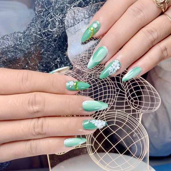 Green almond-shaped nails with white floral and gold accents.