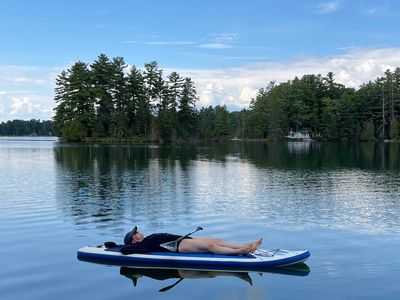 Julia relaxes on a paddle-board that is floating on a lake. The sky above is reflected in the lake. 