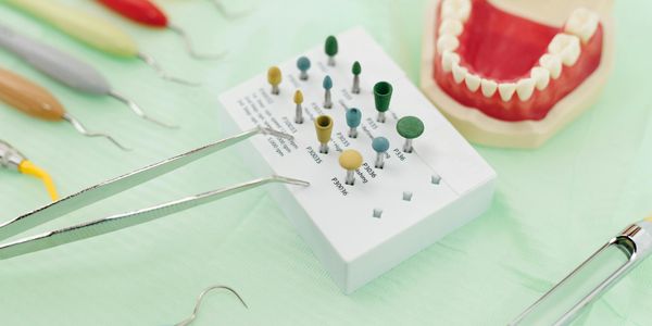 Dental tools and polishing heads with a dental model on a green surface.