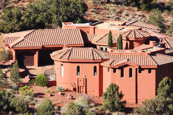 An orange-red adobe-style house with terra cotta tile roofs, nestled in a desert landscape