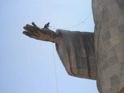 Person rappelling down a large statue's outstretched hand.