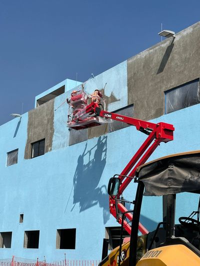 Workers painting a building's exterior using a red hydraulic lift.