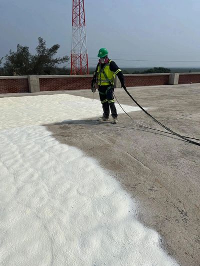 Worker spraying white foam insulation on a flat rooftop.