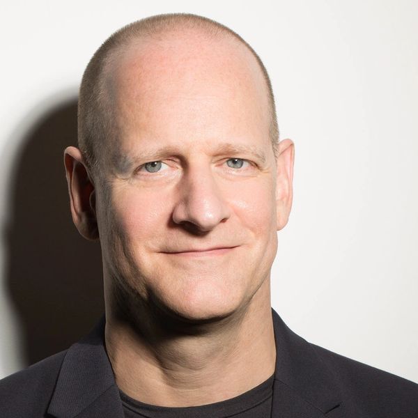 Smiling bald man in a black blazer against a white background.