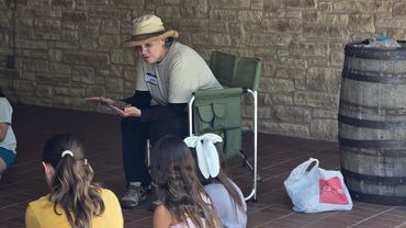 An NTAS volunteer sits in a chair and speaks with a camper.