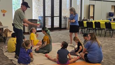 An NTAS volunteer shows an artifact to campers who are sitting on the floor.