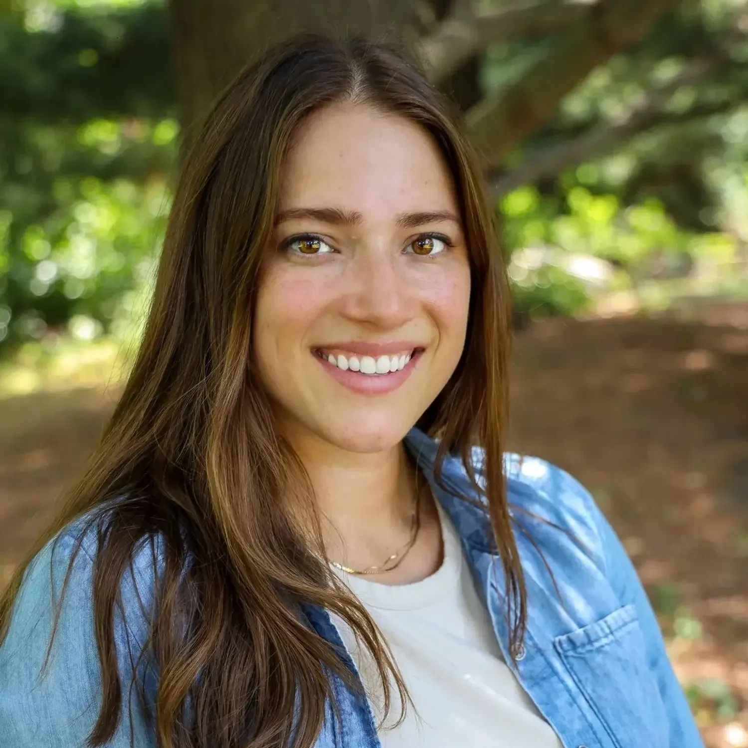 Smiling young woman with long brown hair outdoors.
