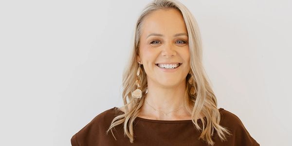 Smiling blonde woman in brown top with long earrings.