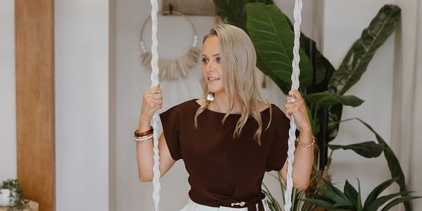 Woman holding onto swing ropes indoors, smiling.