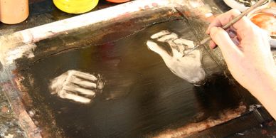 Artist painting detailed hands on a dark canvas.
