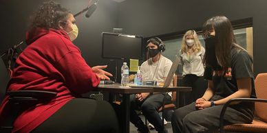 Four masked individuals engaged in a recording session with microphones and headphones.