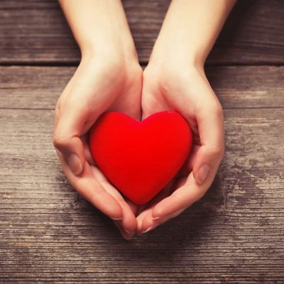 Hands holding a red heart on wooden background.