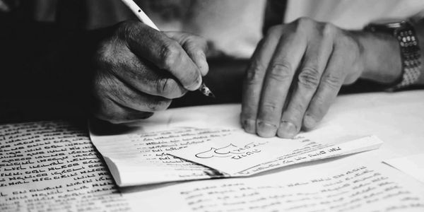 Black and white image of hands writing on papers with a calligraphy pen.
