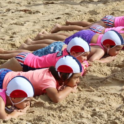 Children lying on the sand in swim caps.