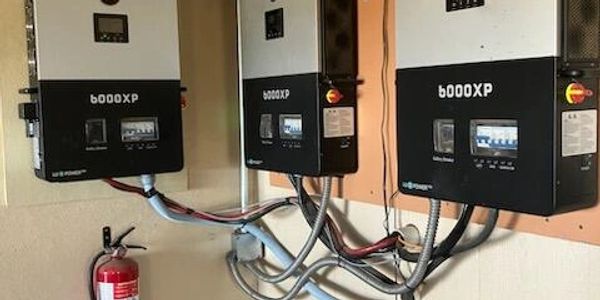 Three EGU b6000XP inverters mounted on a wall with wiring and a fire extinguisher.