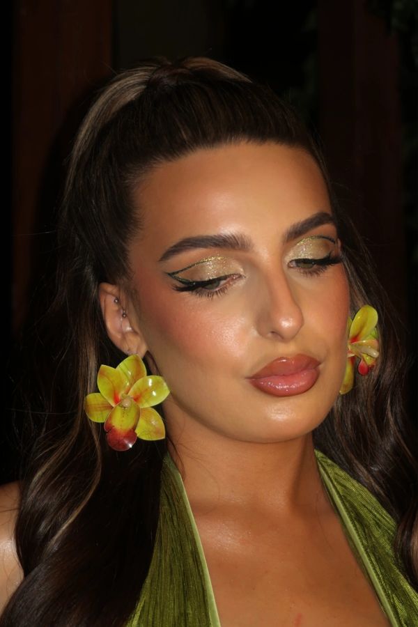 Woman with yellow flower earrings and shimmering eye makeup.