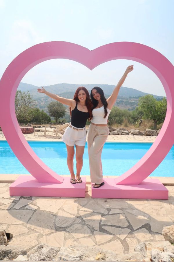 Two women posing happily in a pink heart frame by the pool.