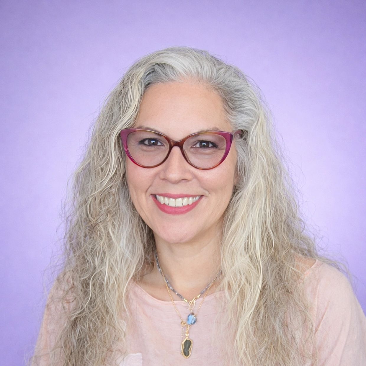 A smiling woman with curly gray hair and purple glasses against a purple background.
