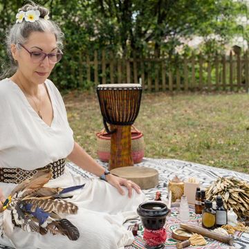 Woman in white dress sitting outdoors with healing items.