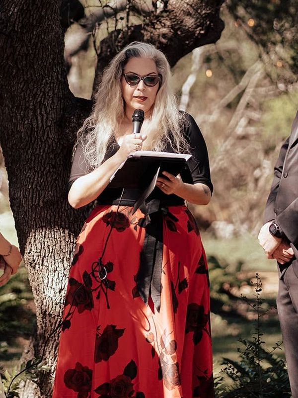 Woman reading from a book with a microphone outdoors.